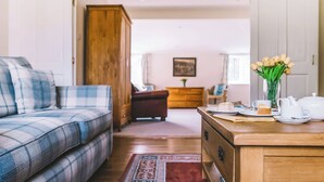 En hyggelig stue med en ternet sofa, et træskab og et spiseområde med et bord dækket til the.
