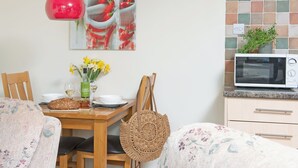 A dining area with a wooden table, chairs, a red hanging light, a microwave, and a wall-mounted painting. - Virginia Cottage - 28108 (Bovey Tracey)