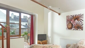 A living room with a sofa, a television, a painting, and a view of a garden through a window. - Virginia Cottage - 28108 (Bovey Tracey)