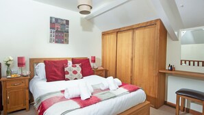 A bedroom with a bed, wooden wardrobe, bedside tables, a mirror, and a ceiling light. - Virginia Cottage - 28108 (Bovey Tracey)