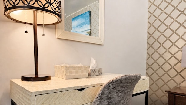 A desk with a lamp, a tissue box, and a chair in a room with a patterned wall and a painting. - Whispering Pines Resort (Grand Bend)
