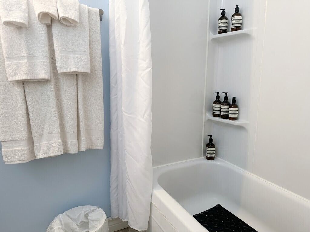 A bathroom with a bathtub, white towels, and toiletries on shelves.