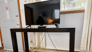 A TV on a dark wooden stand with a cable running to the wall. - Whispering Pines Resort (Grand Bend)