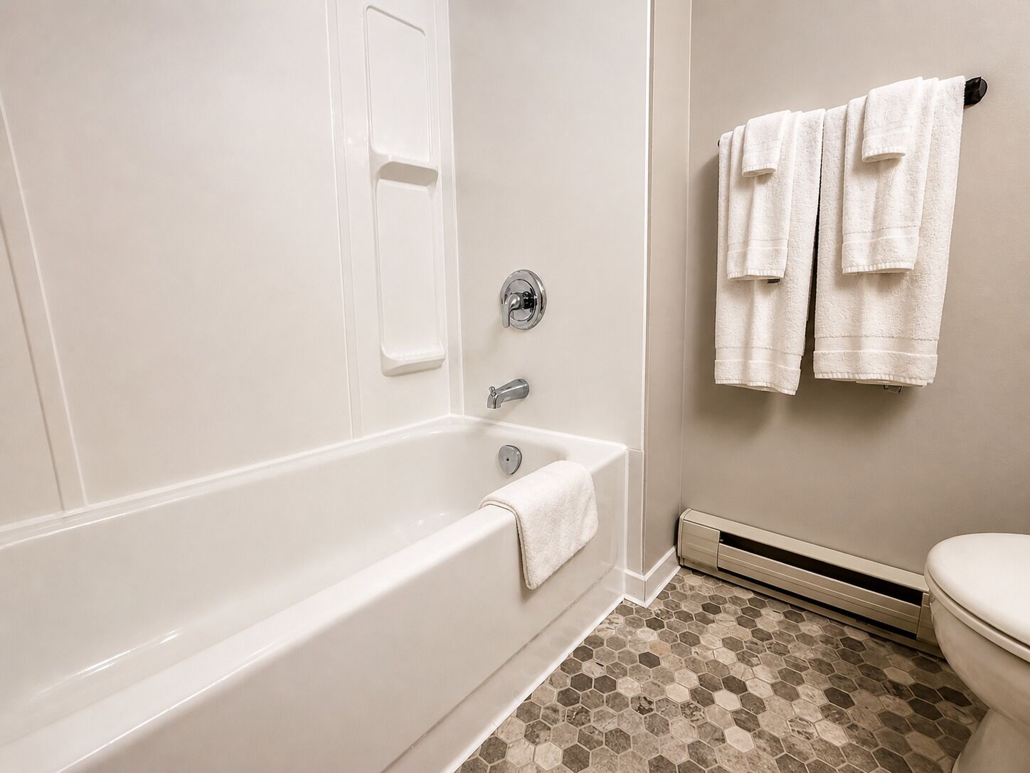 Een badkamer met een wit bad, een toilet en een handdoekrek met handdoeken.