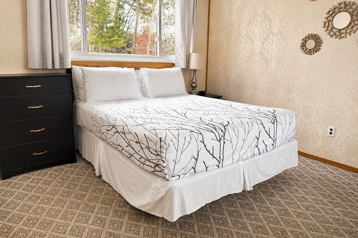 A bedroom with a bed, a dresser, a window with curtains, a lamp, and wall decorations.