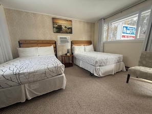 Una habitación de hotel con dos camas, una ventana con vistas, un cuadro en la pared y un cartel de un motel cercano.