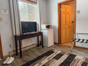 Habitación con televisor, microondas y refrigerador, puerta de madera y alfombra a rayas.