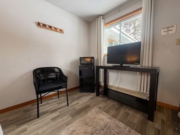 Una habitación con una silla negra, un televisor sobre un mueble, un microondas y un cartel que prohíbe fumar y vapear.