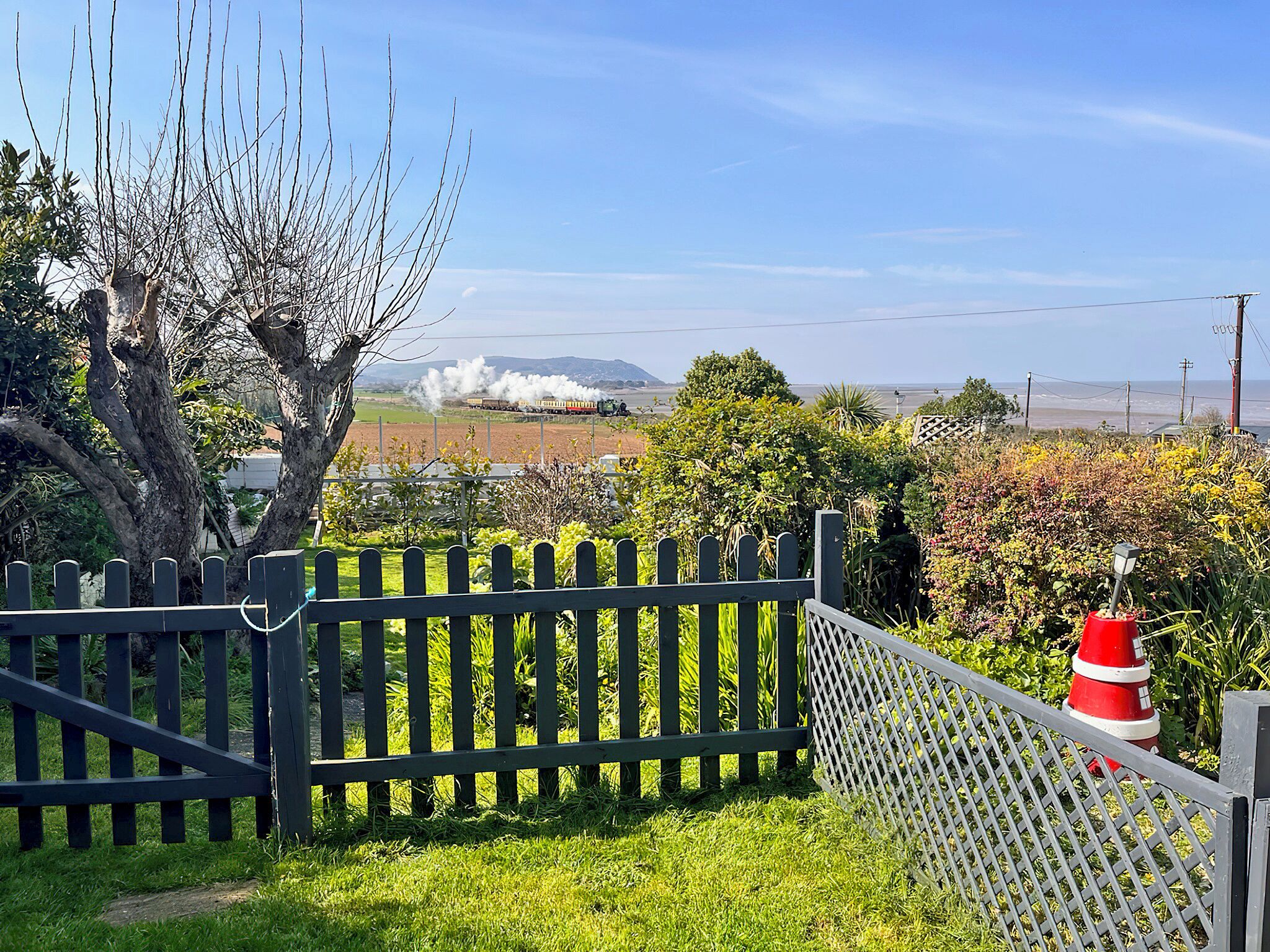 Jardín cercado con vista a un tren a lo lejos.