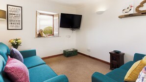 Un salón con sofás color esmeralda, un televisor, una ventana con un peluche de oso y una pared con citas motivacionales.