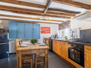A kitchen with wooden cabinets, a dining table set for four, and a Red Bell Tobacco sign. - 2 bedroom accommodation in Marhamchurch, near Bude (Marhamchurch, near Bude)