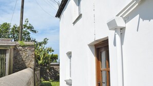 Un bâtiment blanc avec une porte en bois, un mur en pierre et un petit jardin.