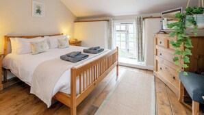 Un dormitorio con cama de madera, una mesita de noche, una planta colgante y vistas al exterior a través de una ventana.