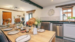 Un comedor con una mesa de madera dispuesta para una comida, una cocina con electrodomésticos modernos y una viga de techo rústica.