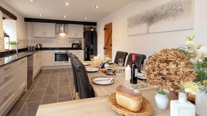 Una cocina moderna con armarios blancos, un comedor con una mesa lista para dos personas y un adorno de pared decorativo.