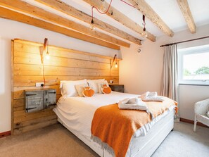 Un dormitorio con cabecera de madera, cama con ropa blanca, una manta y una mesita de noche con espacio de almacenamiento.