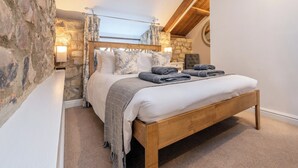 Ein Schlafzimmer mit Steinwand, Holzbettgestell und geneigter Decke.