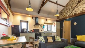 A cozy living room with a sofa, a dining table with chairs, a kitchen area with a stove and microwave, and a stone wall. - 2 bedroom accommodation in Marhamchurch, near Bude (Marhamchurch, near Bude)
