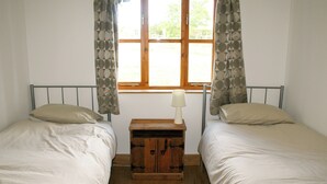Et soveværelse med to enkeltsenge, et trænatbord med lampe, og et vindue med gardiner.