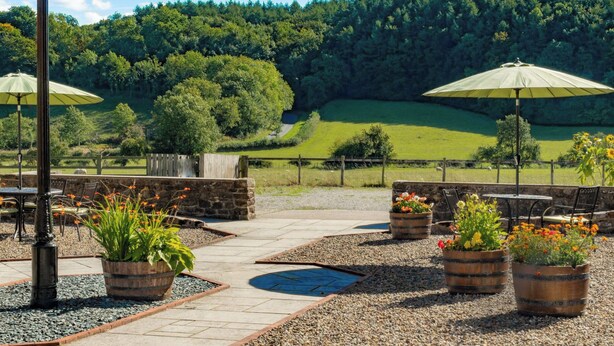 An outdoor patio area with stone flooring, wooden planters with flowers, and umbrellas providing shade. - 3 bedroom accommodation in Stape, near Pickering (Stape, near Pickering)