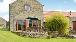 A stone house with a sloped roof, large windows, and a wooden bench outside. - 3 bedroom accommodation in Stape, near Pickering (Stape, near Pickering)