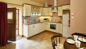 Een compacte keuken met witte kastjes, een magnetron, een oven en een eettafel met stoelen.