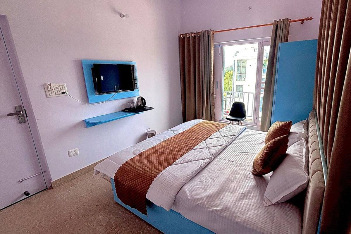 Un dormitorio con cama, televisor montado en la pared, ventana con cortinas y una puerta.