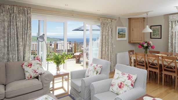 A cozy living room with a sofa, armchairs, and a dining table. A large window offers a view of the outdoors. - 4 bedroom accommodation in Portpatrick (Portpatrick)