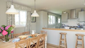 A dining area with a wooden table, chairs, a vase of flowers, and a kitchen in the background. - 4 bedroom accommodation in Portpatrick (Portpatrick)