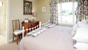 A bedroom with a large bed, a wooden dresser, a chair, and a window with floral curtains. - 4 bedroom accommodation in Portpatrick (Portpatrick)