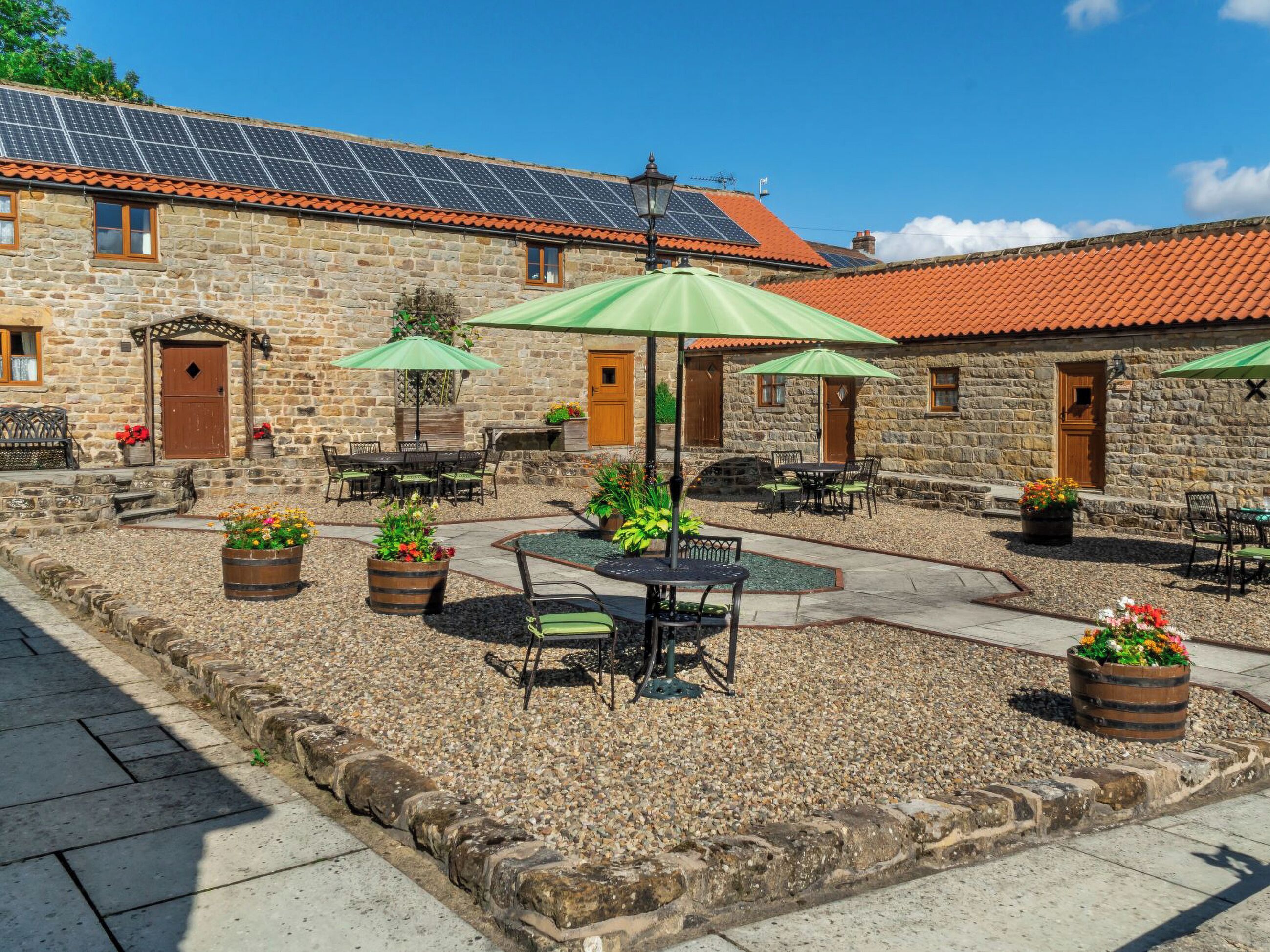Un patio con edificios de piedra, mobiliario exterior y paneles solares en el techo.