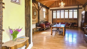 Una habitación amplia con techo de madera y ventanas grandes, una mesa de comedor con sillas y una chimenea.