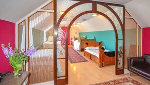 Un dormitorio con cama de madera, pared roja y vista a otra habitación.