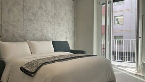 Ein modernes Schlafzimmer mit einem großen Bett, einem dunklen Sessel und Blick auf den Balkon.
