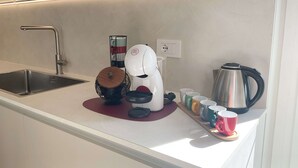 Eine moderne Küche mit einer Spüle aus Edelstahl, einer Kaffeemaschine, einem Wasserkocher und verschiedenen Tassen auf der Arbeitsplatte.