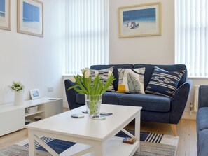 A modern living room with a white coffee table, a blue sofa with patterned cushions, and a framed picture on the wall.
