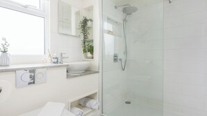 Een moderne badkamer met een douchecabine van glas, een wit wastafelmeubel, toilet en een raam.