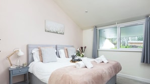 Een slaapkamer met een bed, nachtkastje, lamp en een raam met gordijnen.