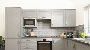 A kitchen with grey cabinets, a microwave, an oven, a sink, and a window. - Little Dunley Cottages - Hazel (Bovey Tracey)
