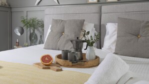 A neatly arranged bedroom with a star decoration, framed pictures, and a bedside table with a lamp, a book, and a bottle. - Little Dunley Cottages - Hazel (Bovey Tracey)