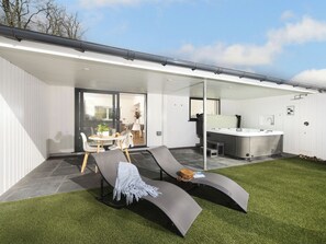 Een modern terras buiten met een zithoek, een jacuzzi en een eethoek.