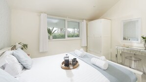 Une chambre d’hôtel avec un lit, une table de chevet, un miroir, une armoire et une fenêtre avec des rideaux.