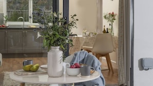 Un coin repas avec une table dressée pour deux personnes, un vase de fleurs et une vue sur la cuisine.