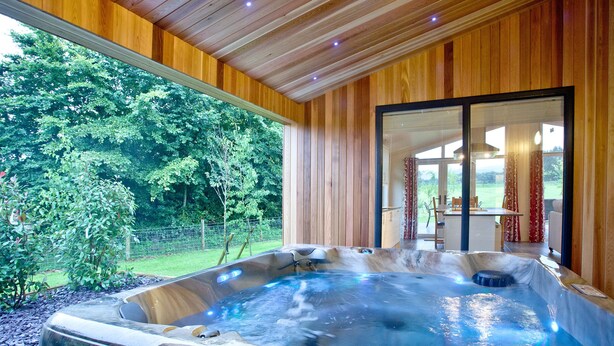 Un bain à remous avec un revêtement extérieur en bois, une porte en verre donnant sur un patio et une vue sur un jardin luxuriant.
