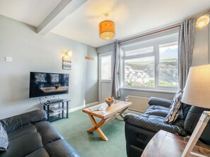 A modern living room with a TV, leather sofa, wooden coffee table, and a large window with a view of the countryside. - Superb sea views from a ground floor apartment, set in tranquil grounds. (Seaton)