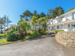 A two-story building with a balcony, surrounded by lush greenery and a stone wall. - A first floor apartment with sea views from the balcony. (Seaton)
