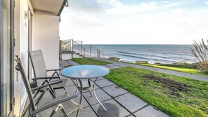 A patio with a table and chairs, a small grassy area, and a view of the ocean. - 1 bedroom accommodation in Seaton (Seaton)