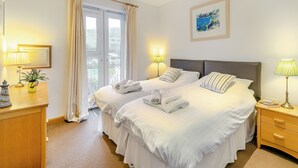 Ett hotellrum med två sängar, en byrå i trä, ett skrivbord med en lampa och ett fönster med gardiner.