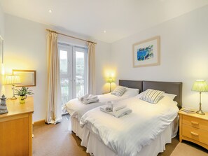 A hotel room with two beds, a wooden dresser, a desk with a lamp, and a window with curtains. - 2 bedroom accommodation in Seaton (Seaton)