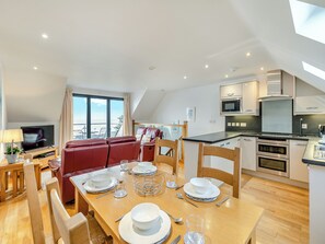 A modern living room with a dining area, a red sofa, and a kitchen with stainless steel appliances. - 2 bedroom accommodation in Seaton (Seaton)